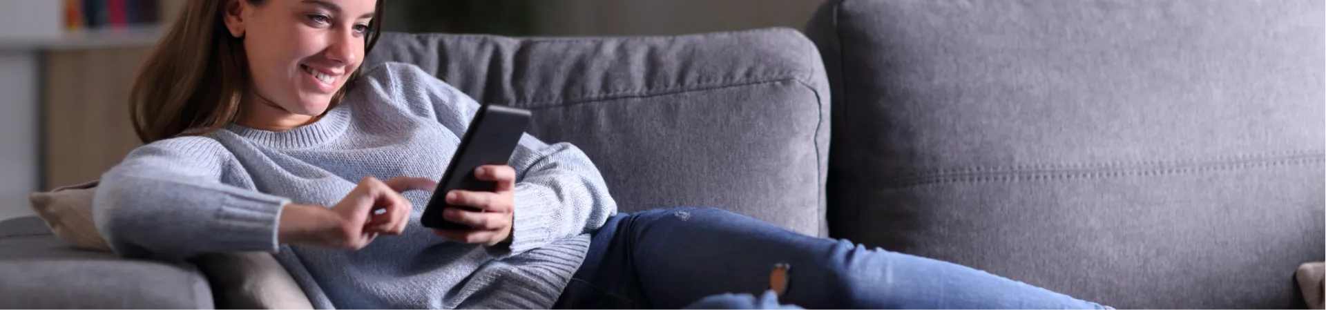 mulher deitada sofa segurando celular Mulher deitada em um sofa cinza segurando celular